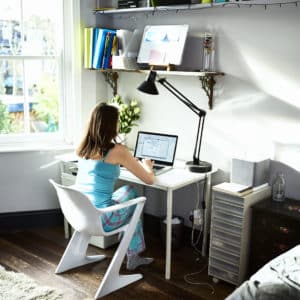 Woman sitting at desk in bedroom using laptop