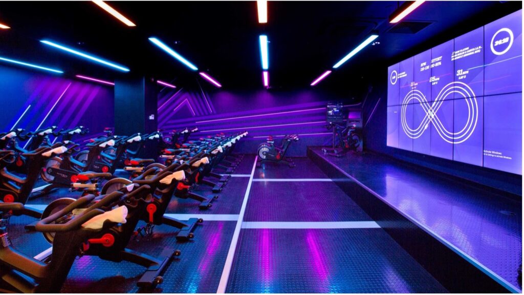 A Virgin Active cycle gym studio in front of a large LED video screen wall. 